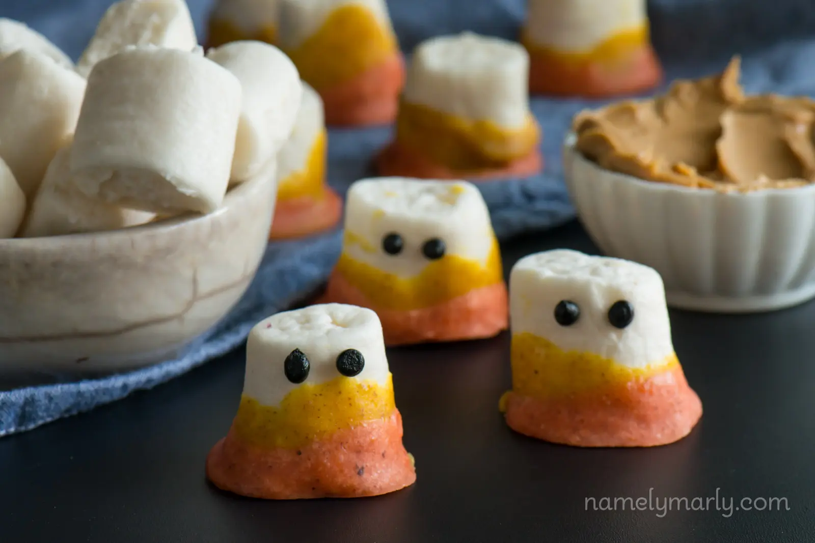 The ingredients to make Vegan Candy Corn Marshmallow Ghosts are sitting on a dark counter.
