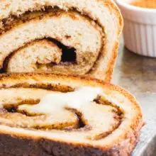 A slice of vegan cinnamon bread with melted vegan butter sits next to the rest of the loaf.