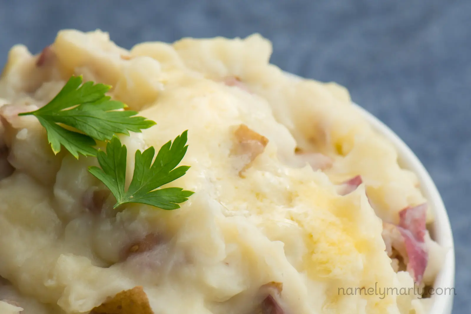a bowl of vegan garlic mashed potatoes with melted butter on top and two parsley sprigs.