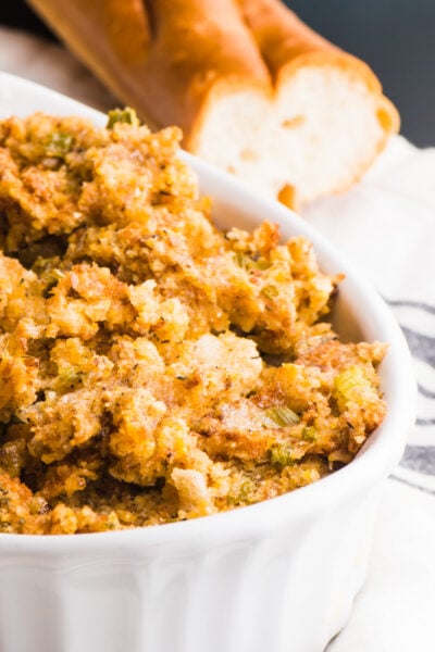 Picture of Vegan Stuffing in a white casserole dish with a loaf of french bread in the background