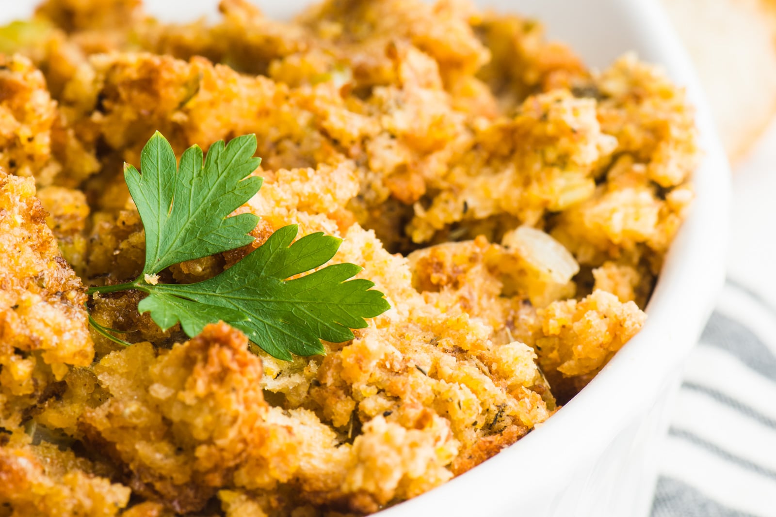 Vegan stuffing is in a white casserole dish and is topped with a fresh parsley sprig.