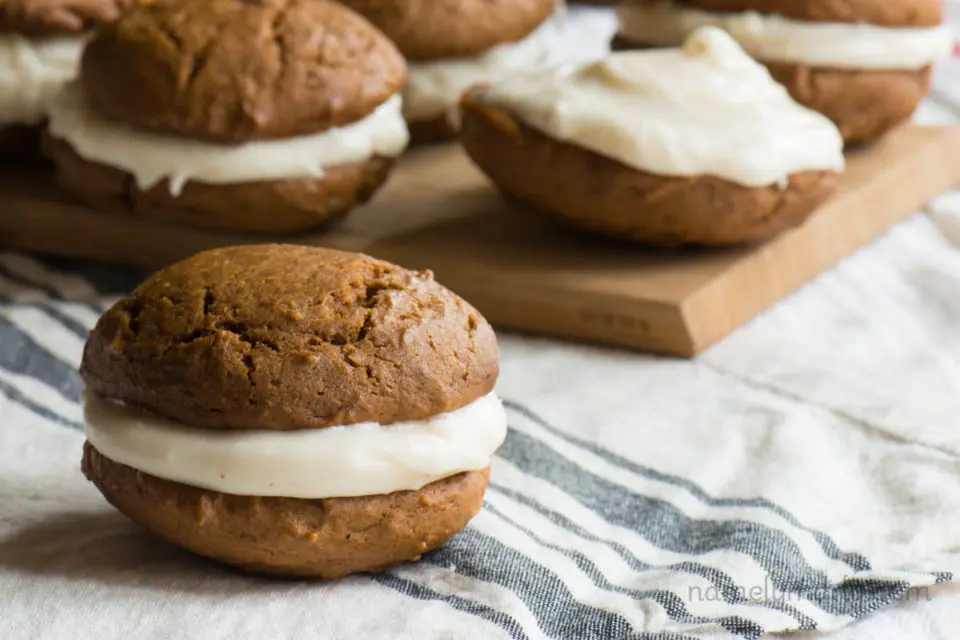 A vegan gingerbread whoopie pie is sitting next to a cutting board with more whoopie pies on it.