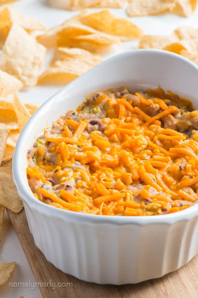 A dish full of vegan dip topped with vegan cheese and surrounded by tortilla chips.  