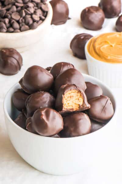 A bowl holds peanut butter balls, one with a bite taken out of it.