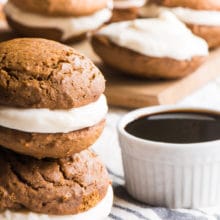 Two vegan gingerbread whoopie pies are stacked on top of each other sitting next to a bowl of syrup.