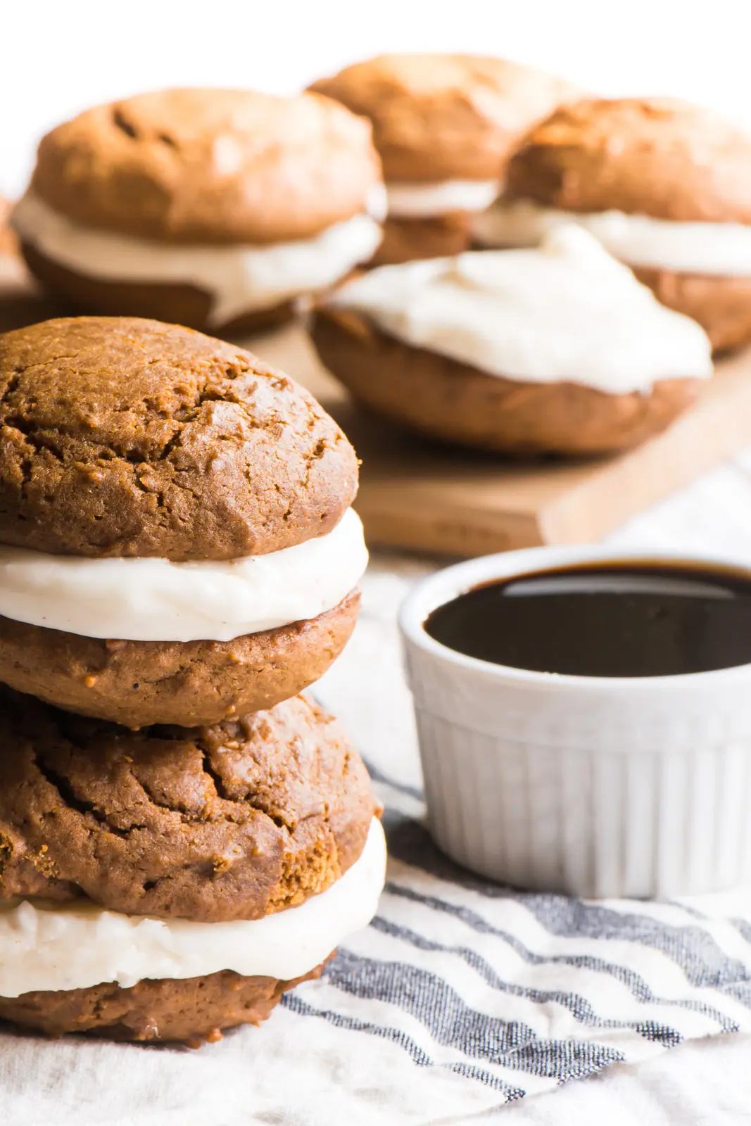 Two vegan gingerbread whoopie pies are stacked and sitting next to a bowl of syrup.