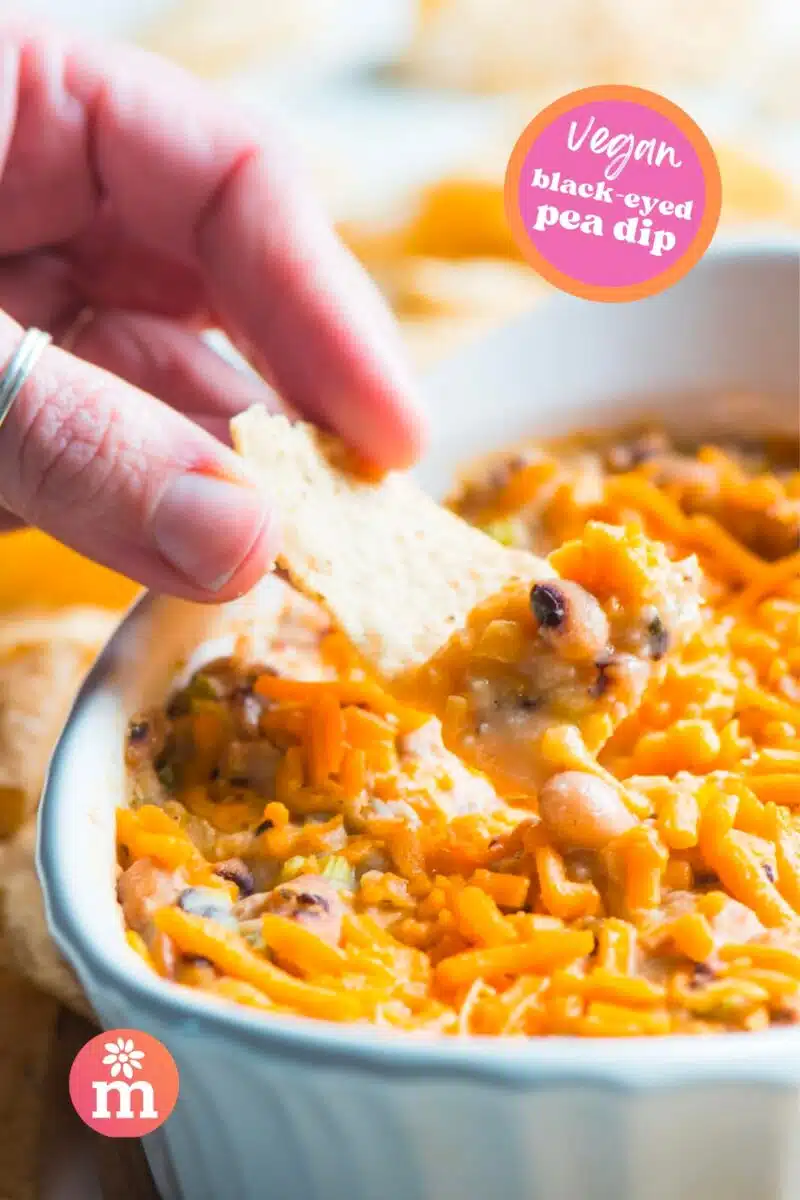 A hand holds a tortilla with dip, hovering over a casserole dish with the rest of the dip. The text reads, Vegan Black-Eyed Pea Dip.