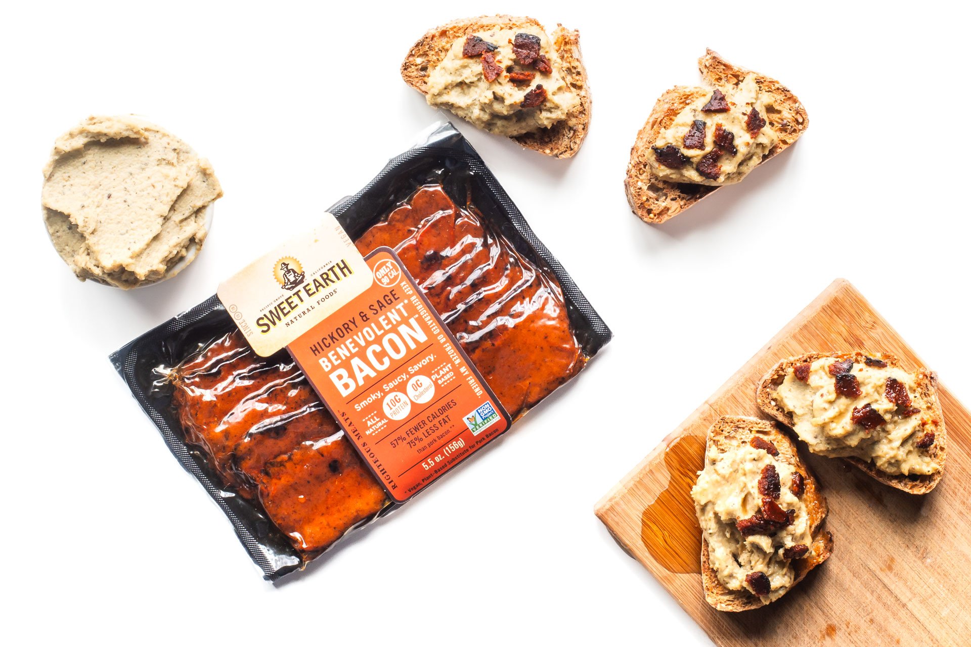 Looking down on a package of vegan bacon, vegan ricotta, and several slices of vegan ricotta bacon crostini.