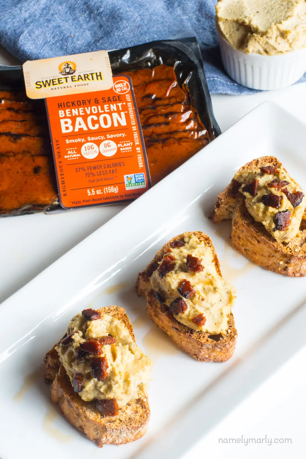 Several slices of vegan crostini are on a plate with a package of vegan bacon behind it.