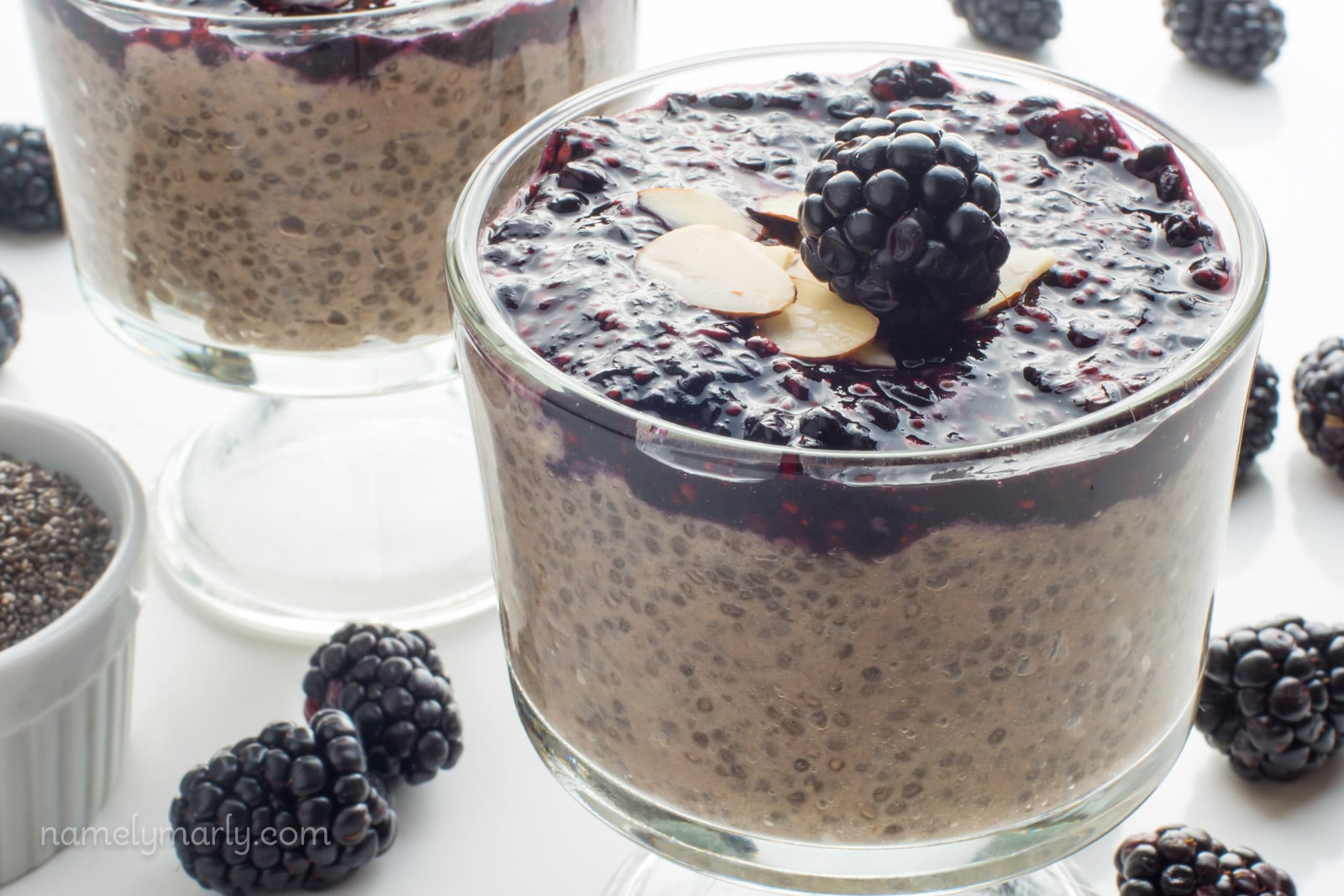 A glass serving dish holds bananas chia pudding with blackberry sauce on top.