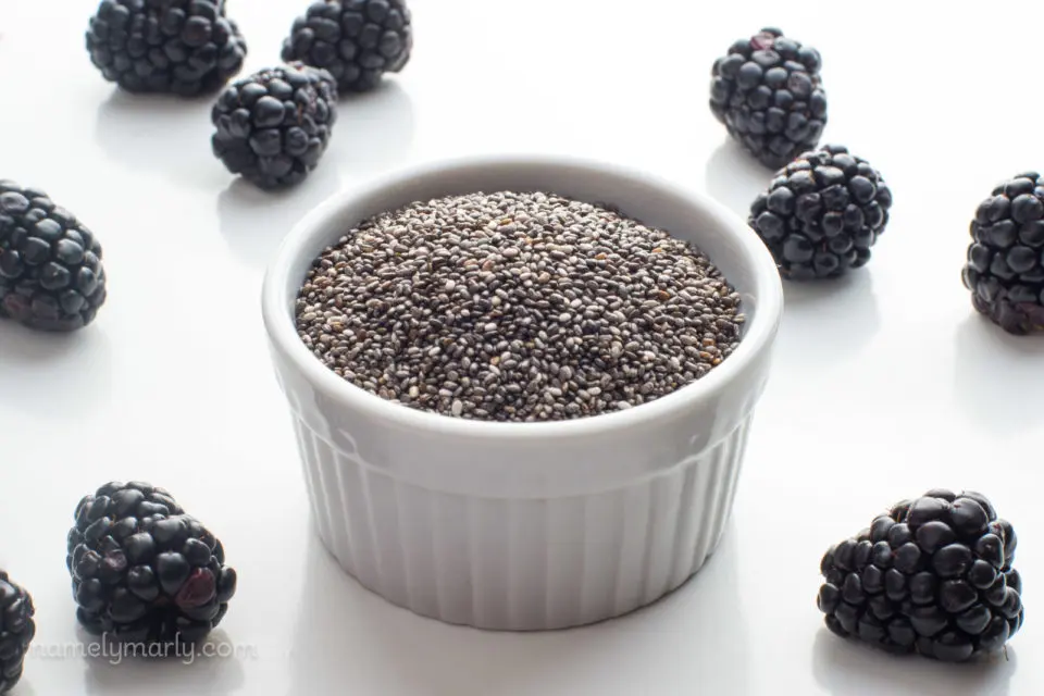 A small bowl of chia seeds sits next to fresh blackberries.