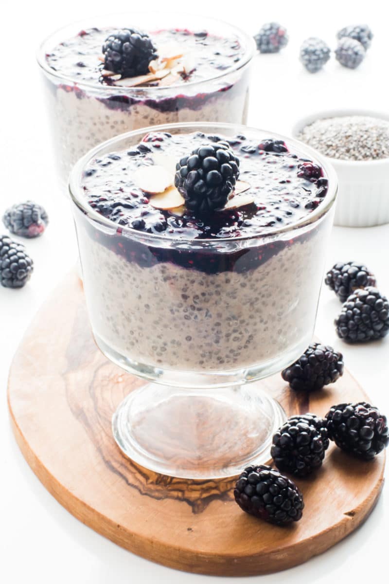 Two serving bowls with vegan banana chia pudding has blackberry sauce on top and fresh blackberries and sliced almonds.