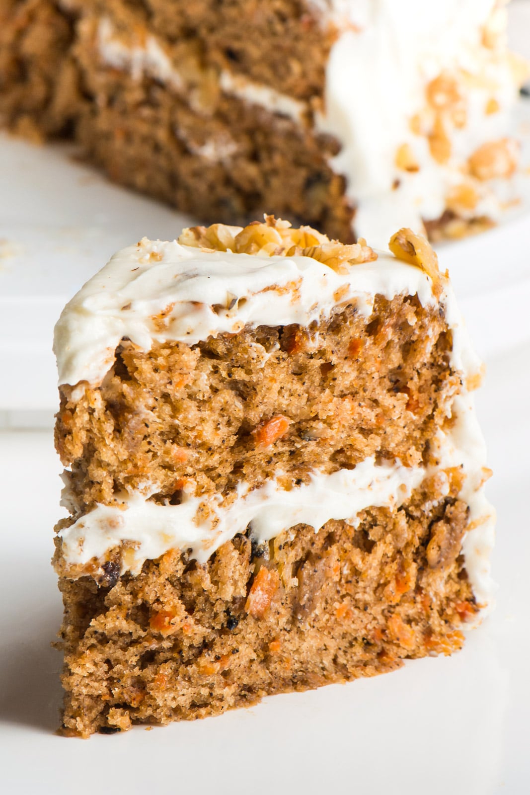 A slice of Vegan Carrot Cake sits in front of the rest of the cake.