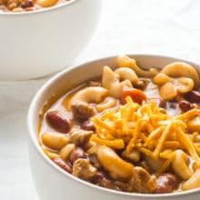 A bowl is full of Vegan Chili Mac with vegan cheese on top. Another bowlful sits behind it.