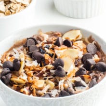 A bowl of vegan German chocolate overnight oats with a bowl of raw oatmeal and a bowl of chocolate chips behind it.