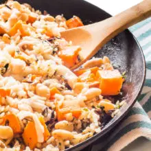A skillet full of wild rice and sweet potato skillet dinner with a wooden spoon in it.