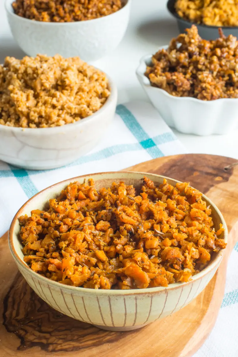 A bowl of Vegan Sweet Potato Sausage Crumbles sits on a cutting board in front of bowls of other vegan sausage substitutes.