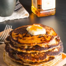 A stack of vegan whiskey pancakes with a pat of butter on top and maple syrup drizzling down the sides.