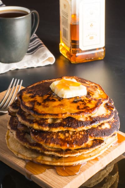 A stack of vegan whiskey pancakes with a pat of butter on top and maple syrup drizzling down the sides.