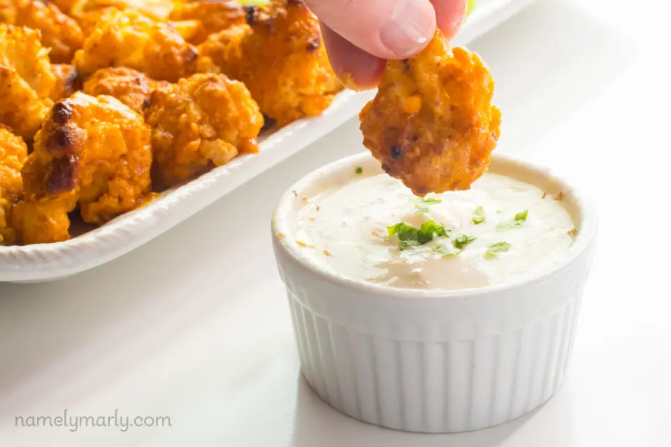 A hand dips Vegan Baked Cauliflower Wings into a bowl of ranch dressing.