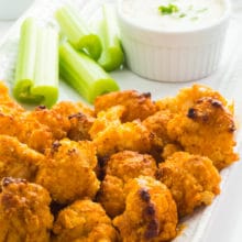 A serving dish with vegan baked buffalo cauliflower wings with sliced celery sticks and ranch dressing.
