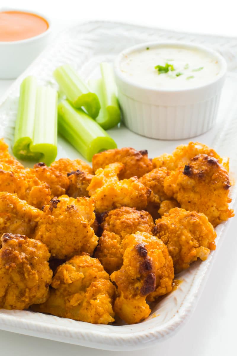 A serving dish with vegan baked buffalo cauliflower wings with sliced celery sticks and ranch dressing.