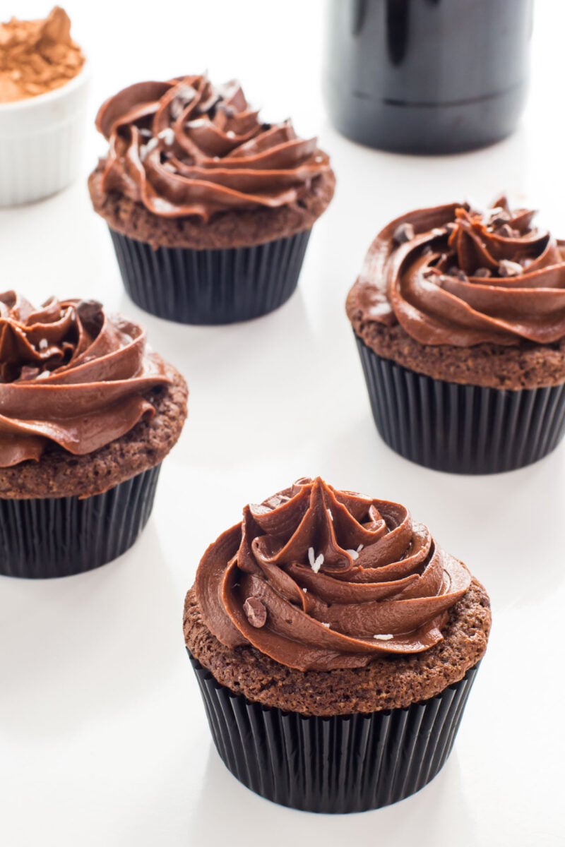 Several chocolate stout cupcakes sitting on a white table with a stout beer behind them.