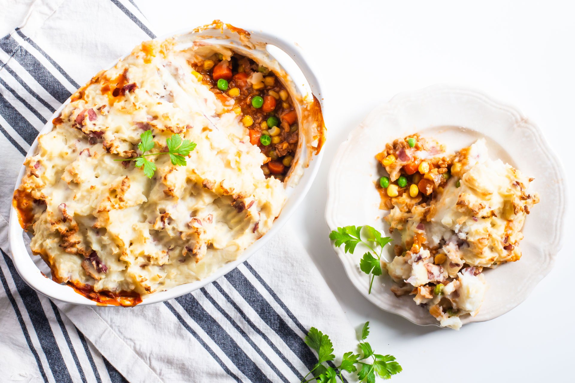 Looking down on a casserole dish full of vegan shepherd's pie with a plate beside it full of a single serving.