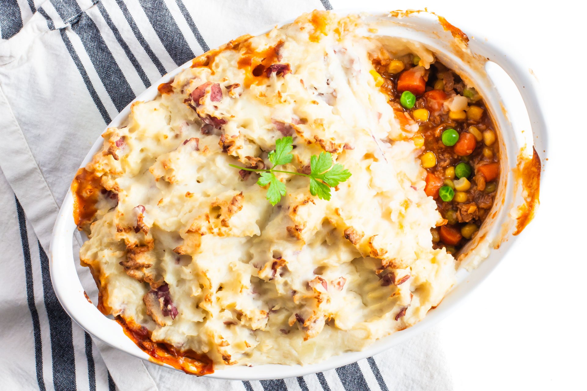 Looking down on a casserole dish with vegan shepherd's pie, and one serving removed.