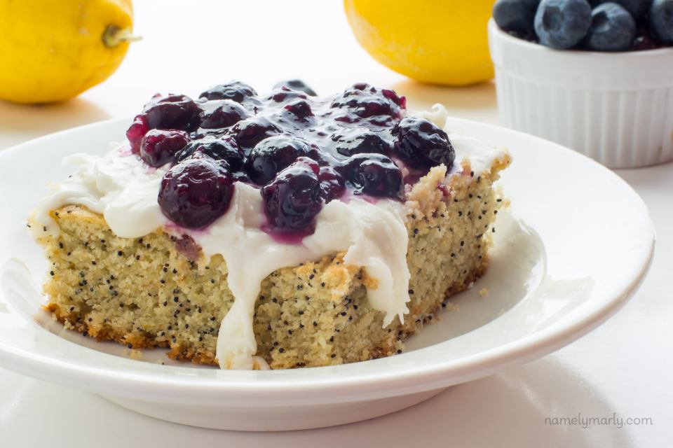 A slice of Lemon Avocado Cake with Blueberry Topping sits in front of lemons and fresh blueberries.