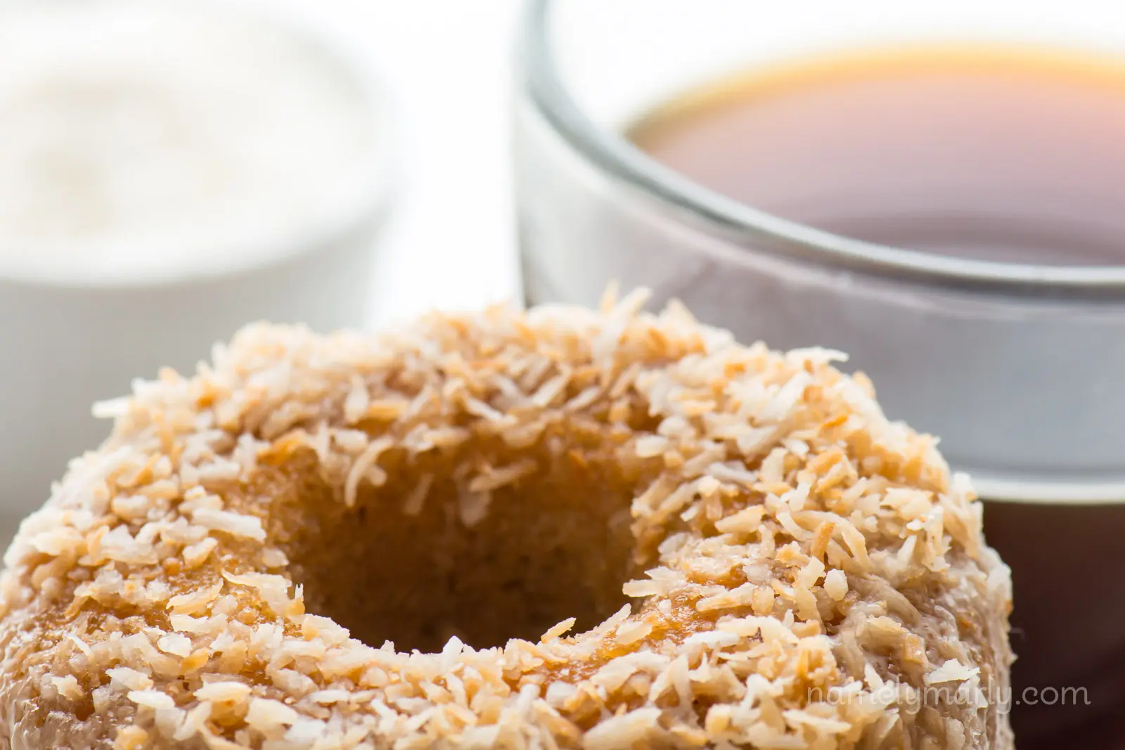 A closeup shot of coconut donuts with a cup of coffee behind them.
