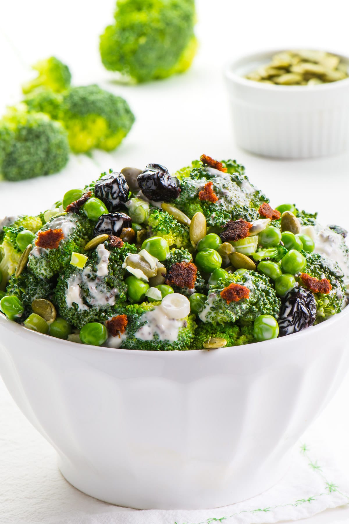 a bowl of Vegan Broccoli Salad with pumpkin seeds in the background and more broccoli.