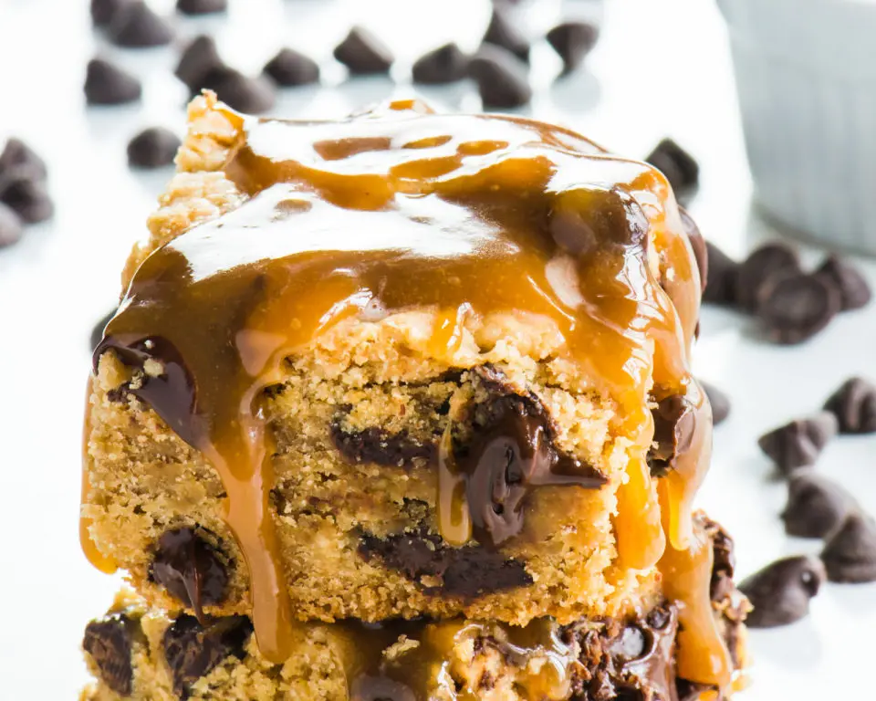 A stack of vegan caramel chocolate chip cookie bars with melted caramel drizzled over the top.