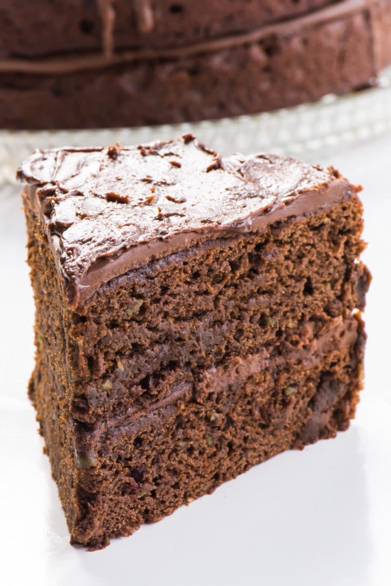 A slice of chocolate cake sits next in front of the rest of the cake.