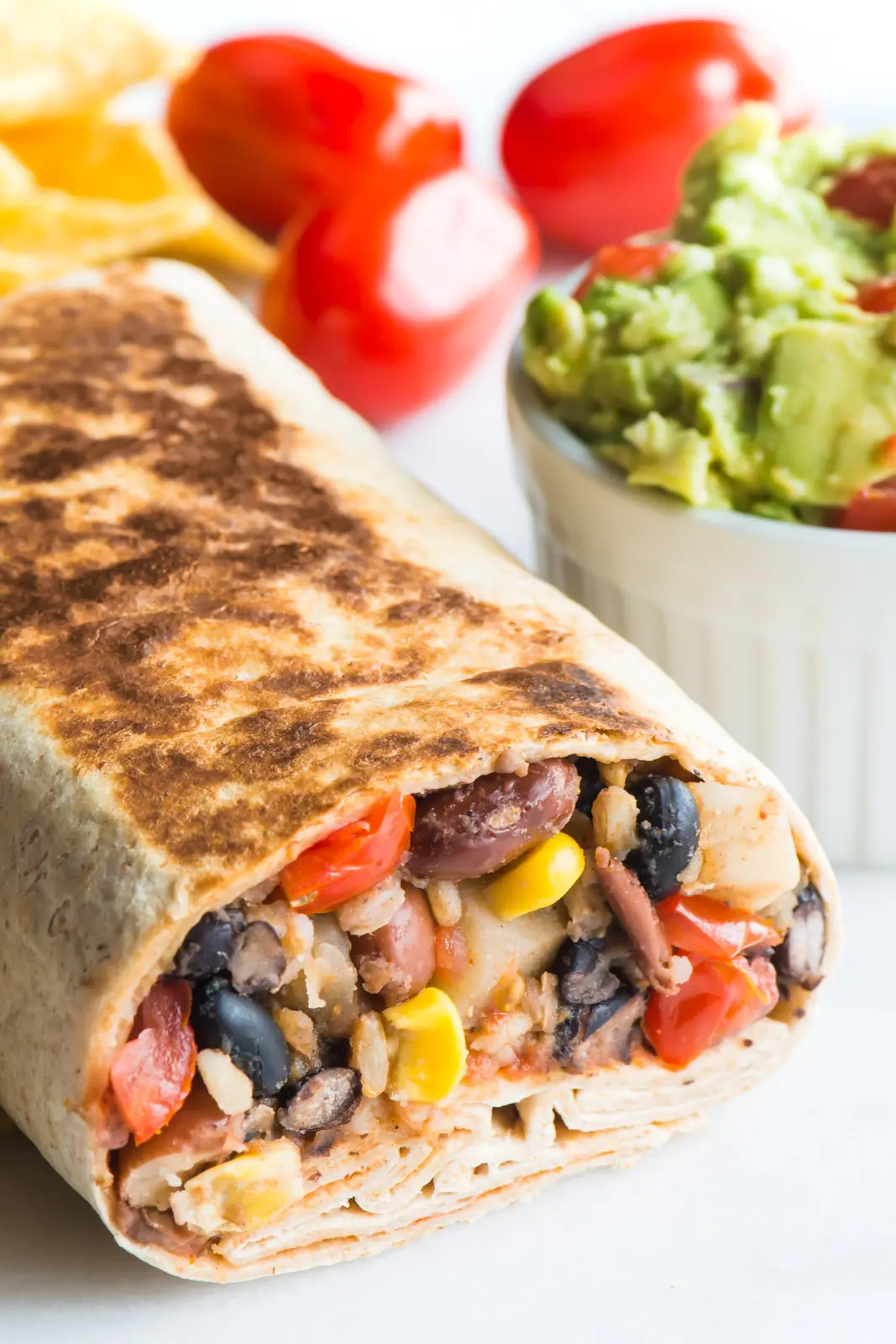 A crispy black bean burrito sits next to a bowl of guacamole and fresh cherry tomatoes.