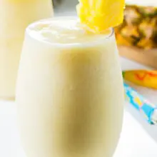 A pina colada cocktail has a piece of pineapple on the glass with a fresh pineapple behind it.