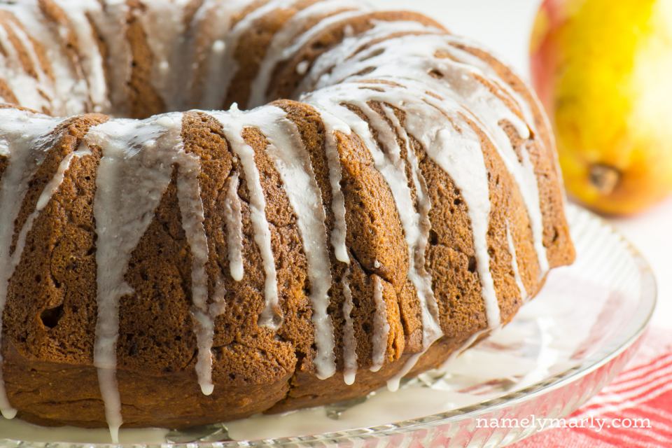 A bundt cake with white icing sits next to a pear.