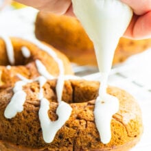 A hand holds an icing bag and is drizzling icing over Vegan Baked Ginger Pear Donuts