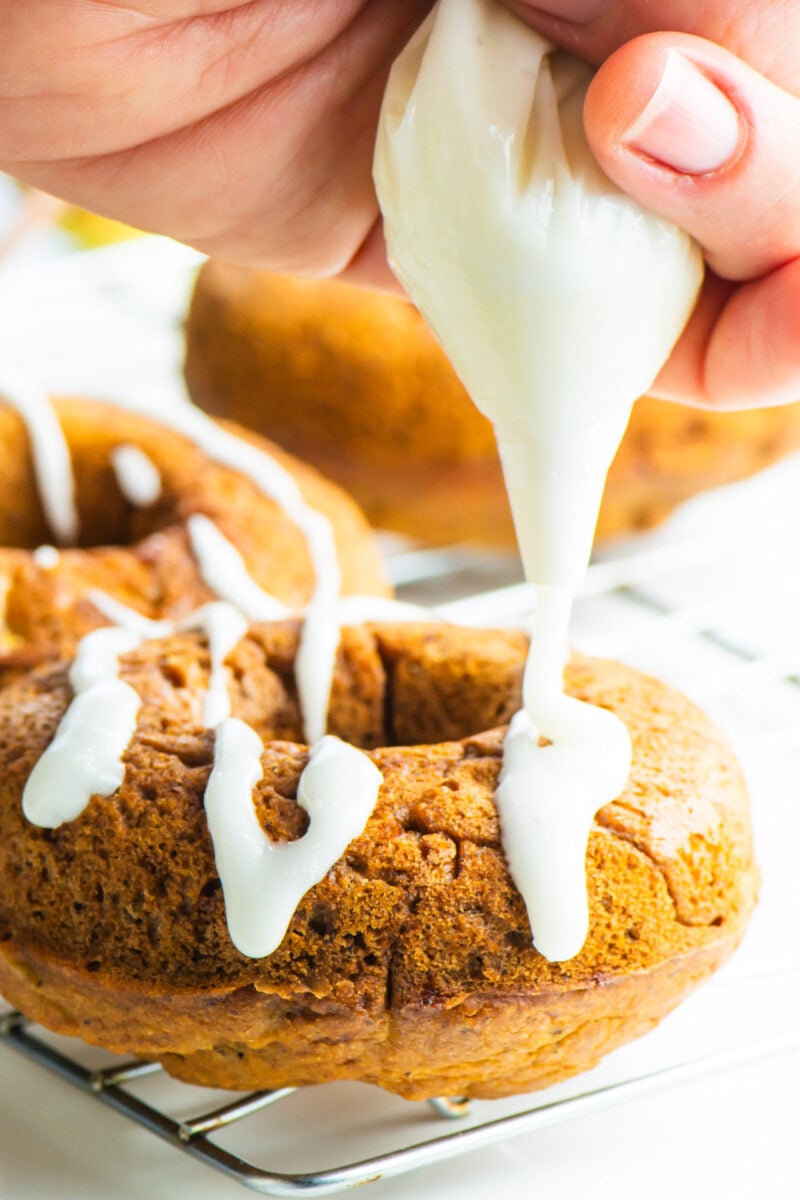 A hand holds an icing bag and is drizzling icing over Vegan Baked Ginger Pear Donuts