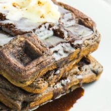 A stack of vegan chocolate waffles on a plate with chocolate syrup and melted vegan butter.