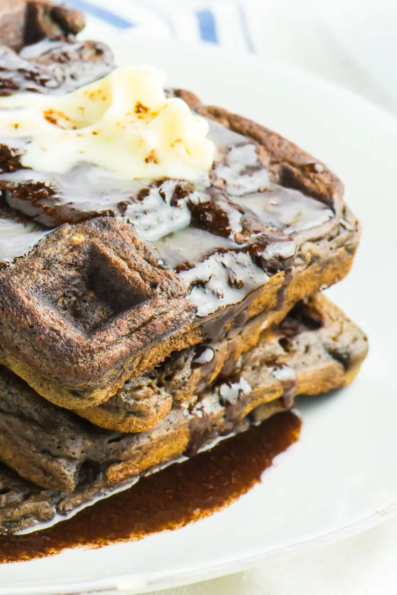 A stack of vegan chocolate waffles on a plate with chocolate syrup and melted vegan butter.