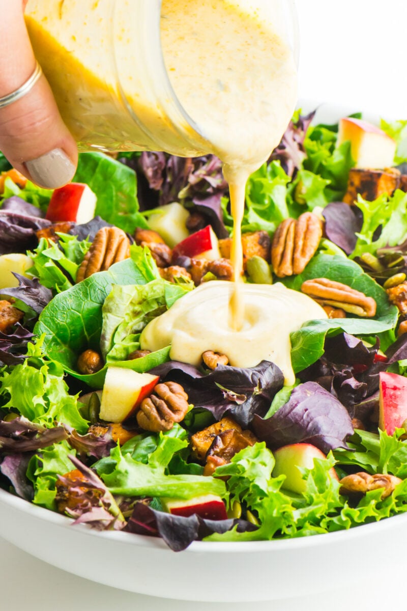 Pouring a jar of pumpkin ranch dressing over a vegan harvest salad.