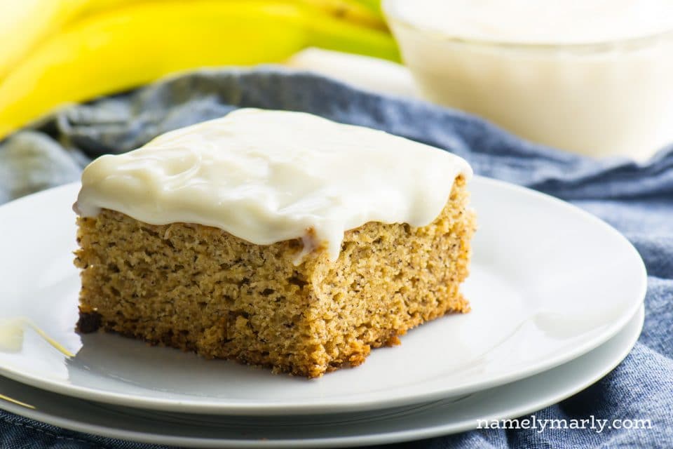 A slice of Vegan Banana Cake sits on a plate in front of bananas.