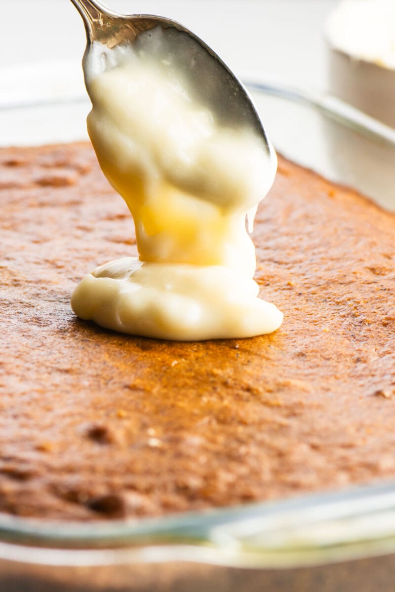 A spoon full of vegan cream cheese frosting is positioned over banana cake.