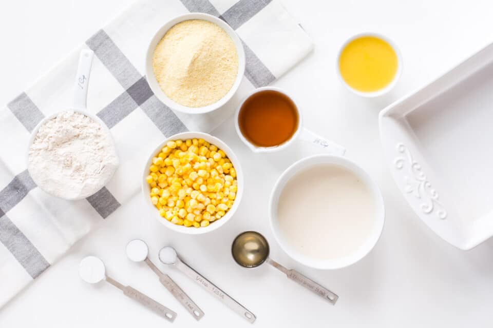 Looking down on ingredients, such as corn in a bowl, cornmeal, flour, melted butter, and more.