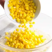 Pouring whole kernel corn into a mixing bowl with flour and cornmeal.