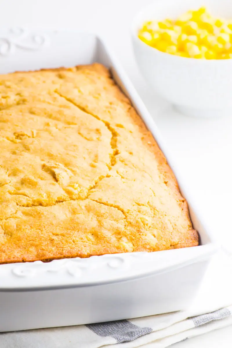 Vegan cornbread in a white baking dish with a bowl of whole kernel corn in the background.