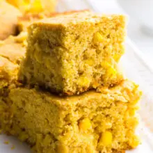 Two slices of vegan cornbread are stacked on top of each other with more slice in the background.
