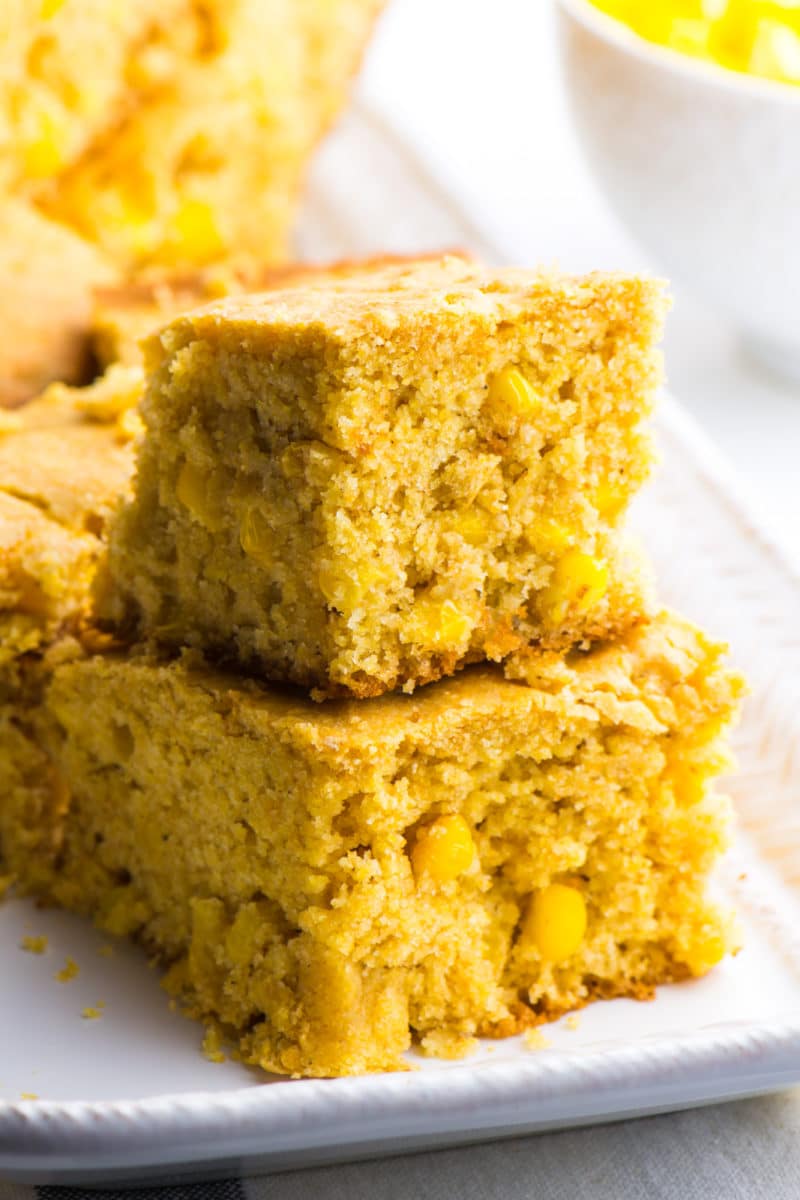 Two slices of vegan cornbread are stacked on top of each other with more slice in the background.