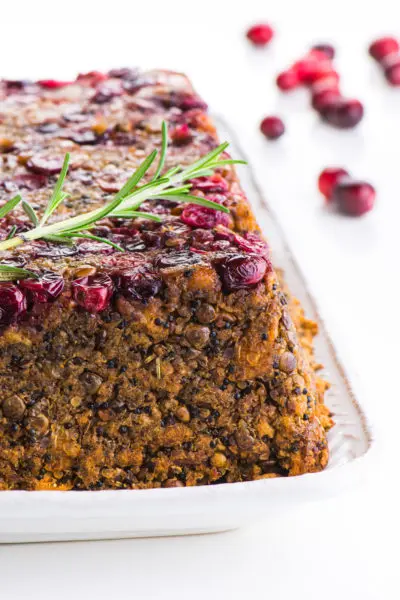 A cranberry-encrusted Lentil Loaf sits on a white plate with cranberries in the background.
